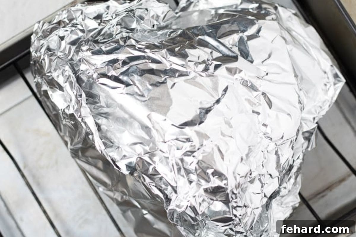 A prepped ham, perfectly wrapped in foil and placed on a roasting rack, resting in a roasting pan filled with water, ready for baking. This setup ensures maximum moisture and flavor.