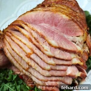 Baked Spiral sliced Ham with Dijon pineapple juice glaze on white platter on top of arugula.