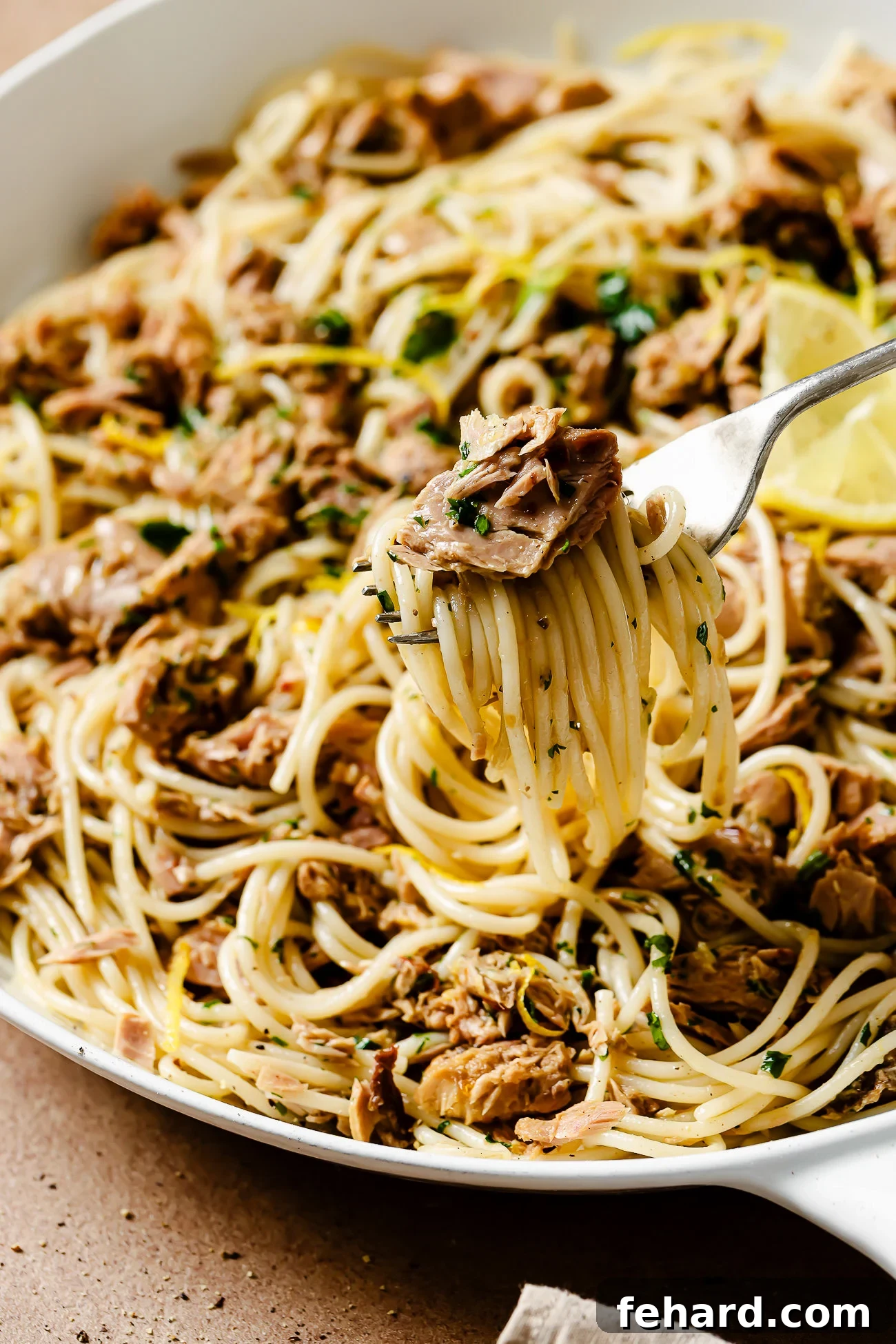 Closeup of a fork twirling delicious tuna pasta, showcasing the flaky tuna, pasta, and fresh herbs.
