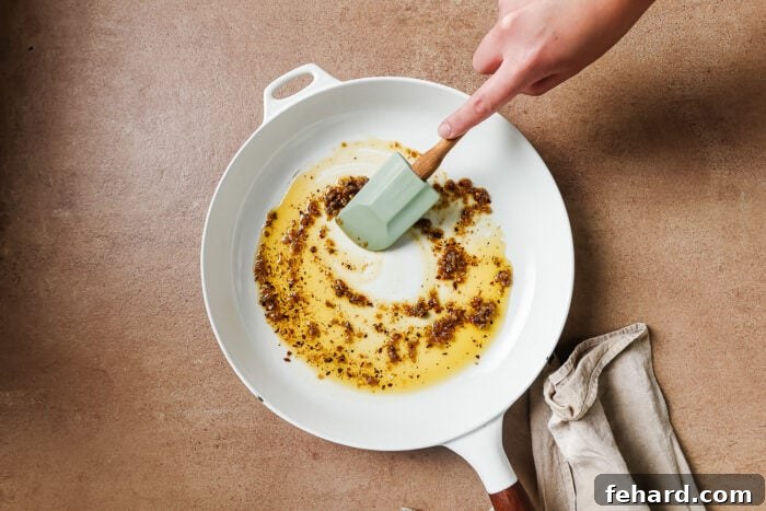 Olive oil gently heating in a white skillet with finely minced garlic, creating an aromatic foundation.