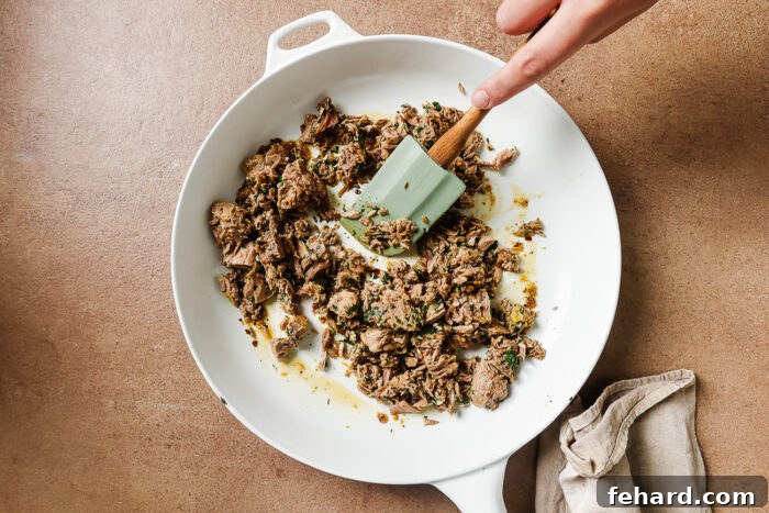 Flaky tuna being gently sautéed in a skillet with garlic-infused olive oil, absorbing all the aromatic flavors.