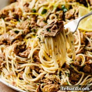 Closeup of a fork twirling tuna pasta in a white bowl, garnished with fresh herbs, ready to be enjoyed.