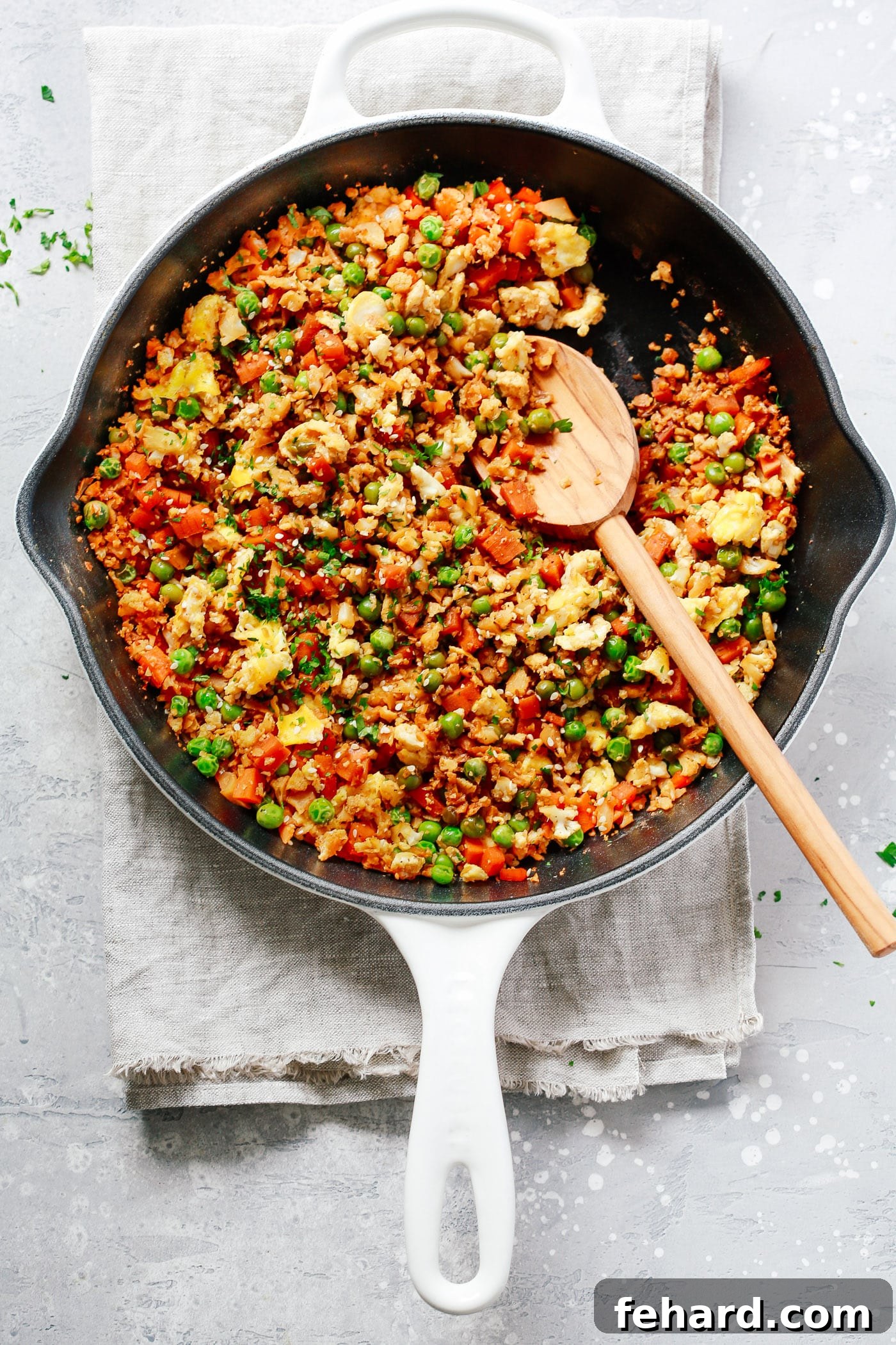 60 Delicious Whole30 Recipes 5 A close-up of fragrant fried cauliflower rice, studded with colorful vegetables, served fresh in a cast iron skillet.
