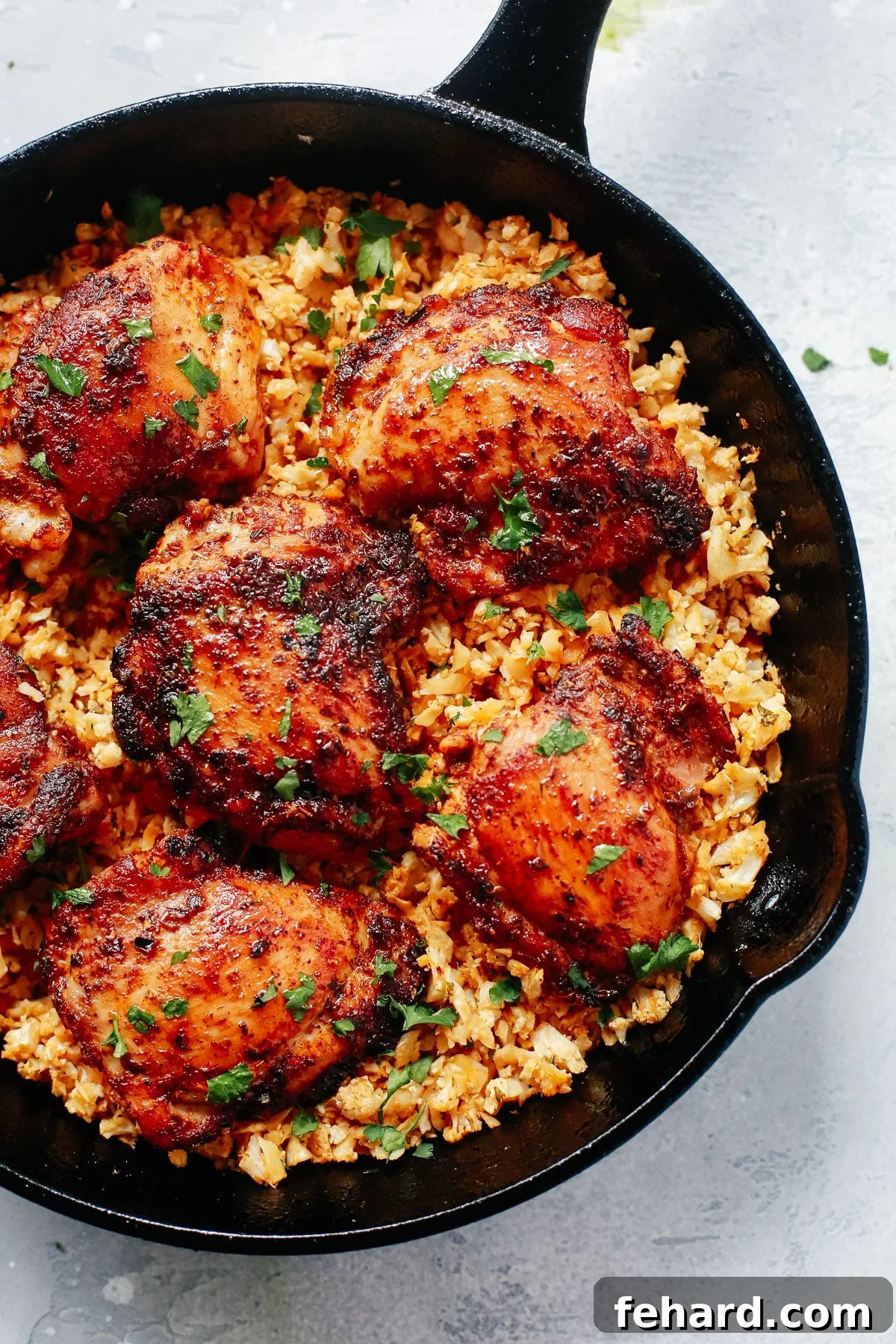 Savory Chicken and Cauliflower Rice 5 Overhead view of a cast iron skillet filled with a hearty serving of chicken and cauliflower rice, garnished with fresh green herbs.