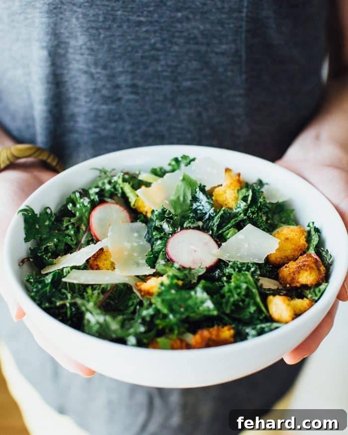 A set of hands holding a bowl of fresh kale caesar salad with cornbread bits, perfect for a picnic.