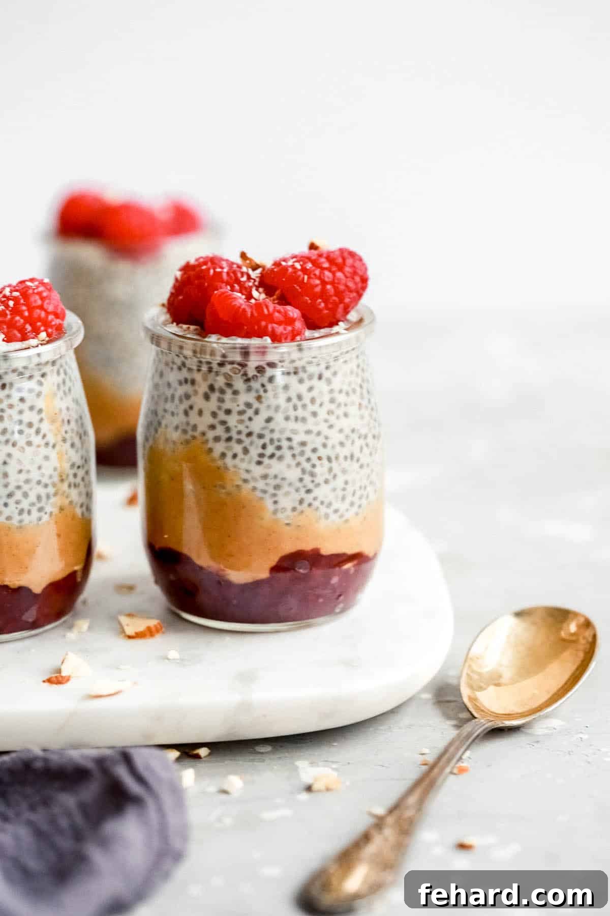Individual glass jars of chia seed pudding topped with fresh raspberries, perfect for a portable sweet picnic treat.