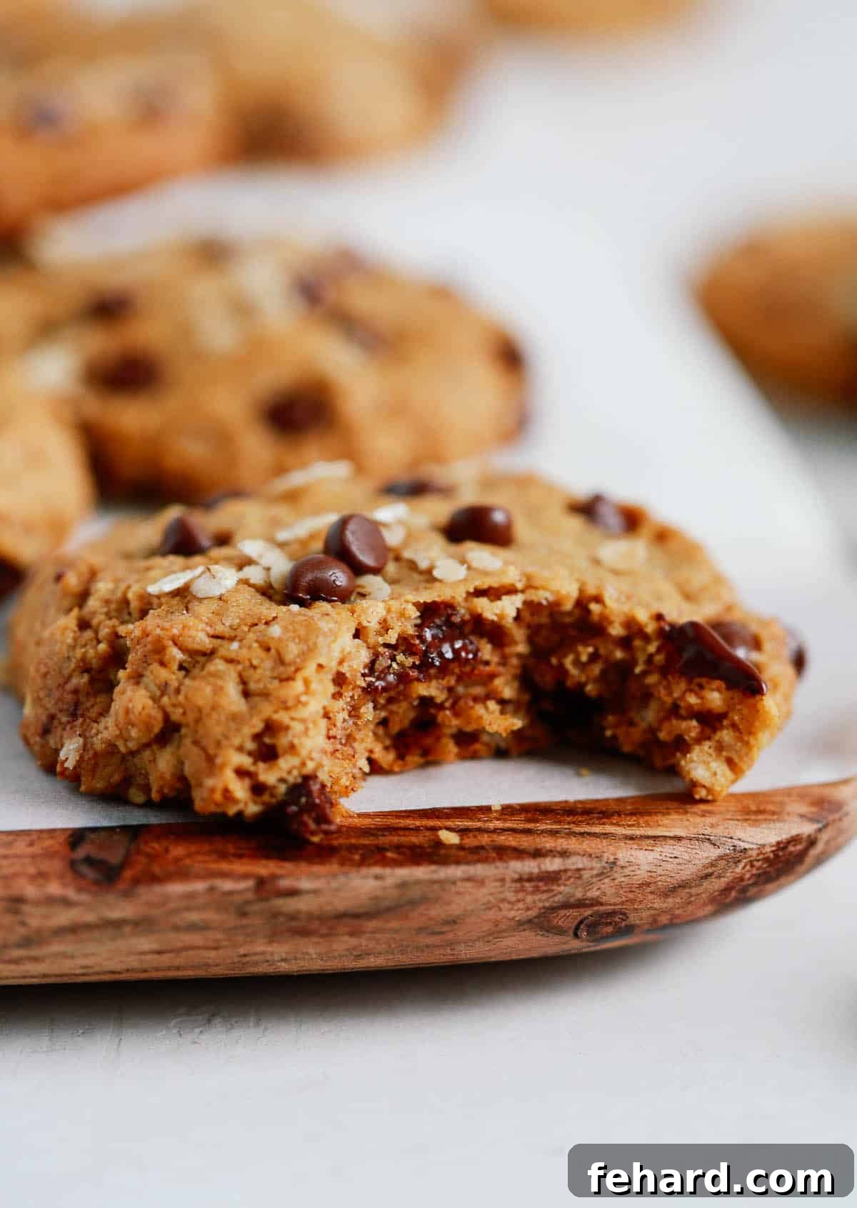 Healthy peanut butter oatmeal cookies with a bite taken out of one, arranged on a wooden serving board.