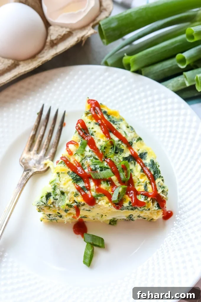 A perfectly sliced Instant Pot Frittata with a drizzle of hot sauce, presented on a pristine white plate, showcasing its golden-brown top and airy texture.