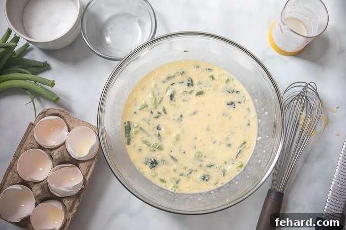 A clear glass bowl filled with whisked egg mixture, including vibrant greens and cheese, ready to be poured into a pan for a Pressure Cooker Frittata.