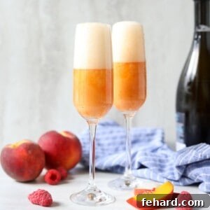 Two glasses of peach bellini cocktails next to fresh peaches and prosecco.