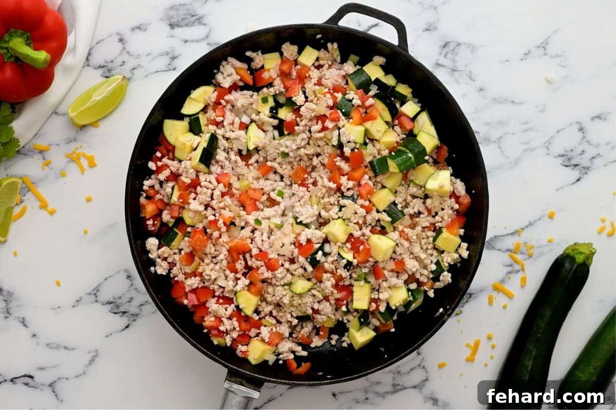 Sautéing Vegetables for Taco Skillet Ground turkey mixed with diced bell peppers, zucchini, and jalapeño sautéing in a skillet, creating a colorful and aromatic base.