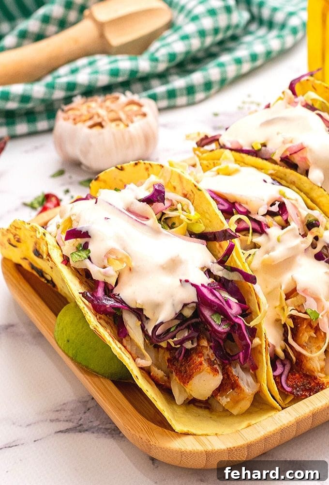 Healthy Fish Tacos with Slaw and Chipotle Sauce Delicious baked fish tacos with fresh cabbage slaw and creamy chipotle sauce, garnished with lime wedges and served on a wooden tray for a healthy and vibrant meal.