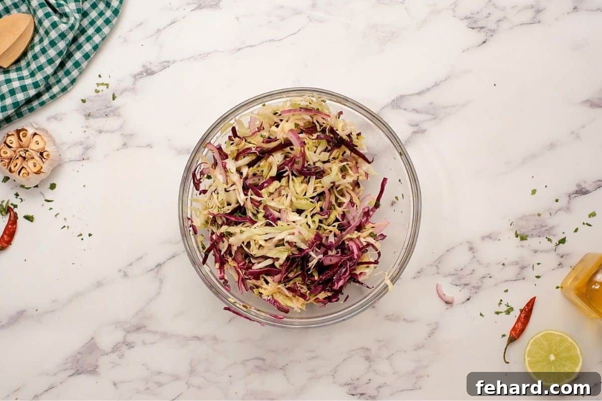 Fresh Fish Taco Slaw Vibrant cabbage lime slaw in a clear mixing bowl, with red onion and cilantro, freshly prepared for healthy fish tacos.