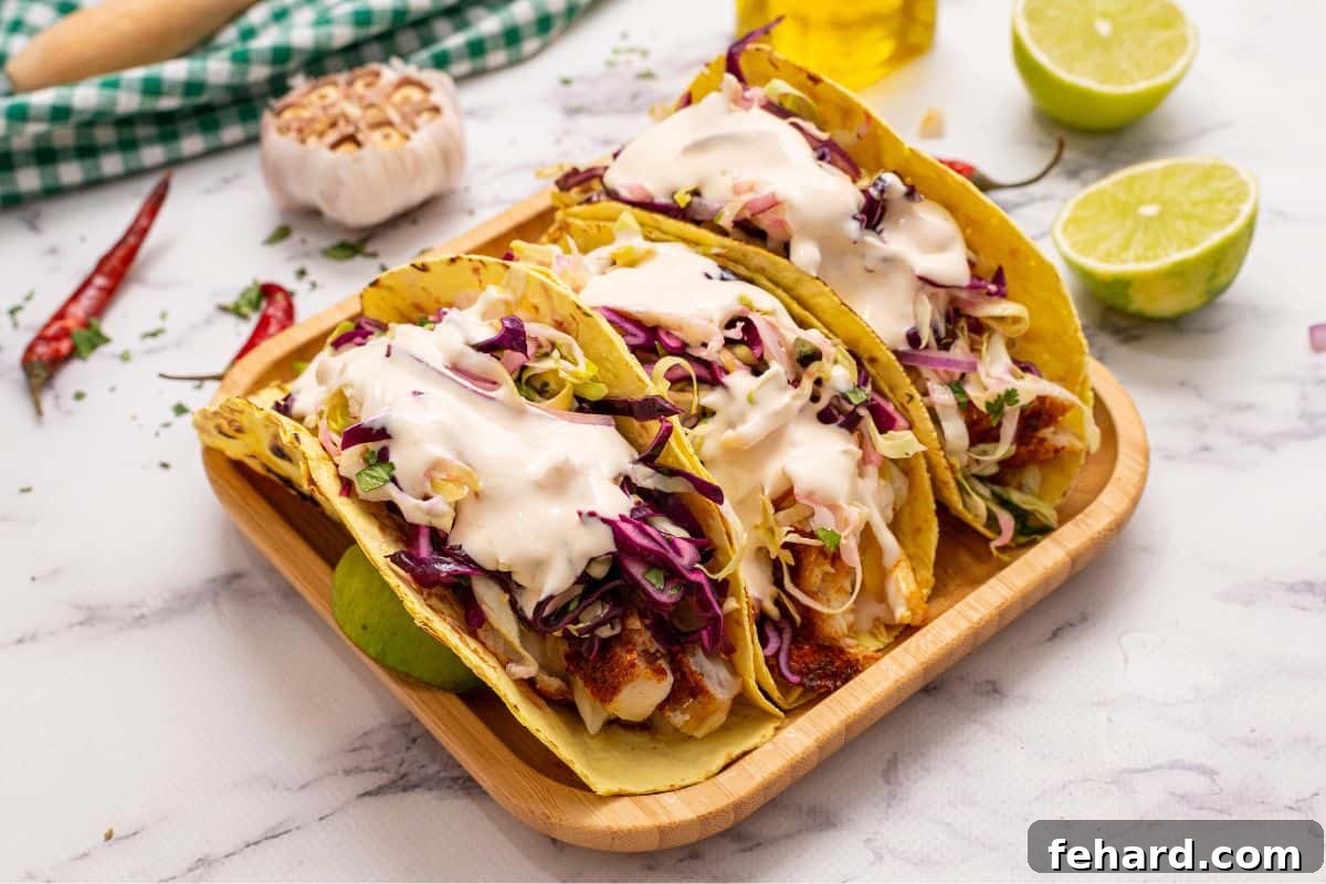 Best Healthy Fish Tacos Ready to Eat Three perfectly assembled healthy baked fish tacos with fresh cabbage slaw and creamy chipotle sauce on warm corn tortillas, garnished with cilantro.