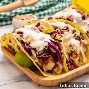 Healthy Fish tacos served with fresh cabbage slaw and creamy chipotle sauce, garnished with cilantro on a light background.