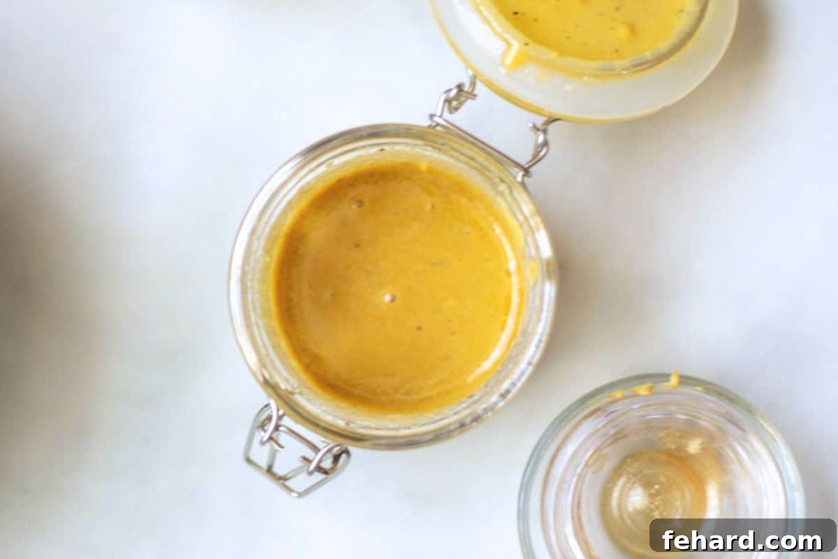 A small glass jar with a lid, filled with a creamy, golden champagne vinaigrette dressing, ready to be used for the holiday salad.