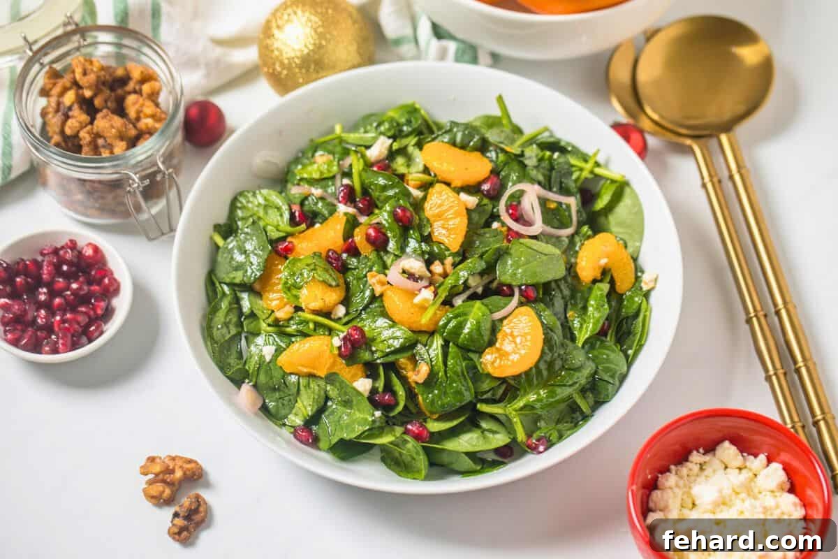 A vibrant Christmas Salad meticulously arranged in a white serving bowl, showcasing layers of fresh baby spinach, bright mandarin oranges, glistening pomegranate arils, crunchy candied walnuts, and crumbled feta cheese, with the elegant champagne vinaigrette dressing.