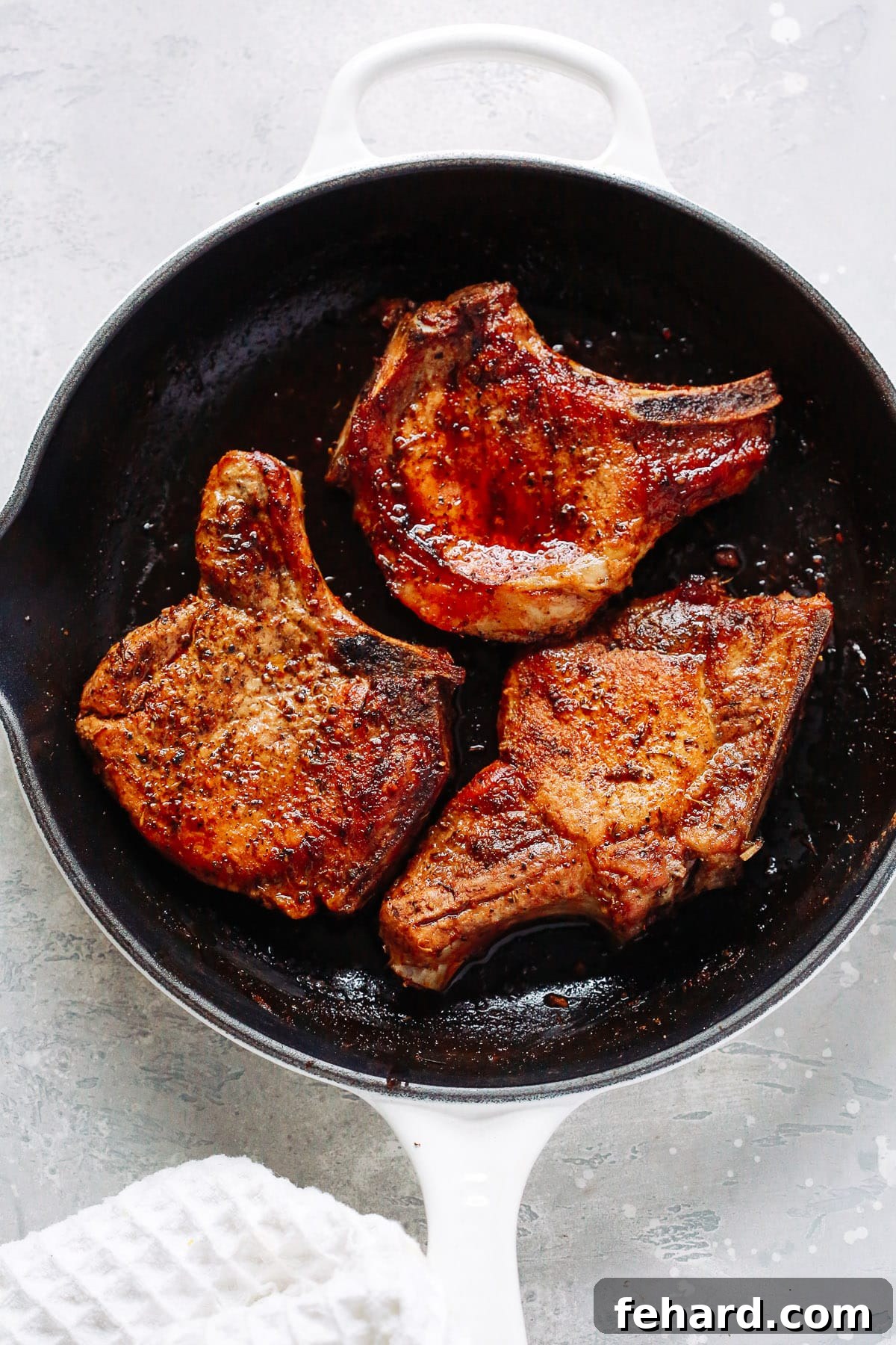 overhead view of a white skillet containing perfectly cooked Oven Pork Chops, garnished with fresh herbs