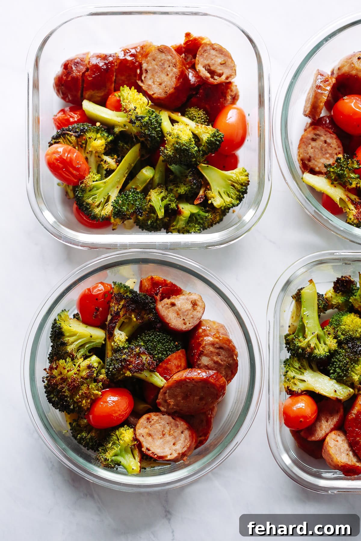 Overhead view of four glass bowls containing Italian sausage and roasted vegetables, ready for meal prep.