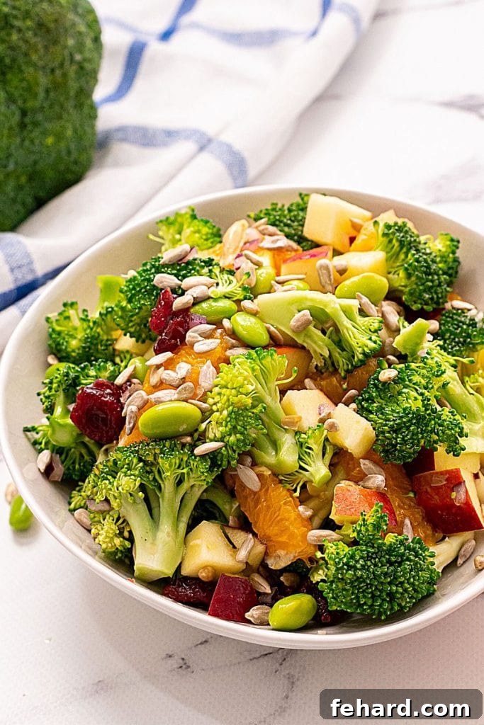 A vibrant Broccoli Apple Salad without mayo, served in a white bowl, with fresh apples and raw broccoli florets arranged artfully on the side. This healthy salad is perfect for any occasion.