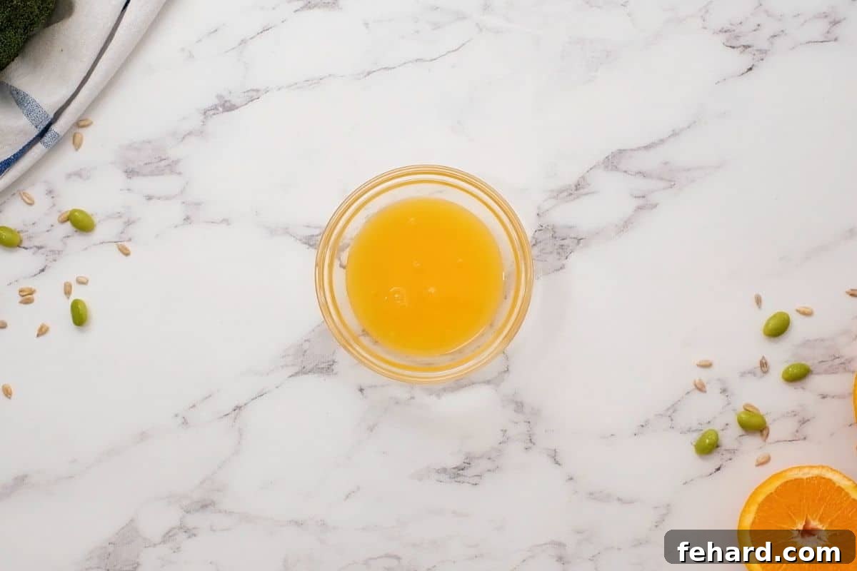 A small glass bowl containing the vibrant orange citrus dressing for broccoli salad, freshly whisked and ready to be drizzled over the ingredients.