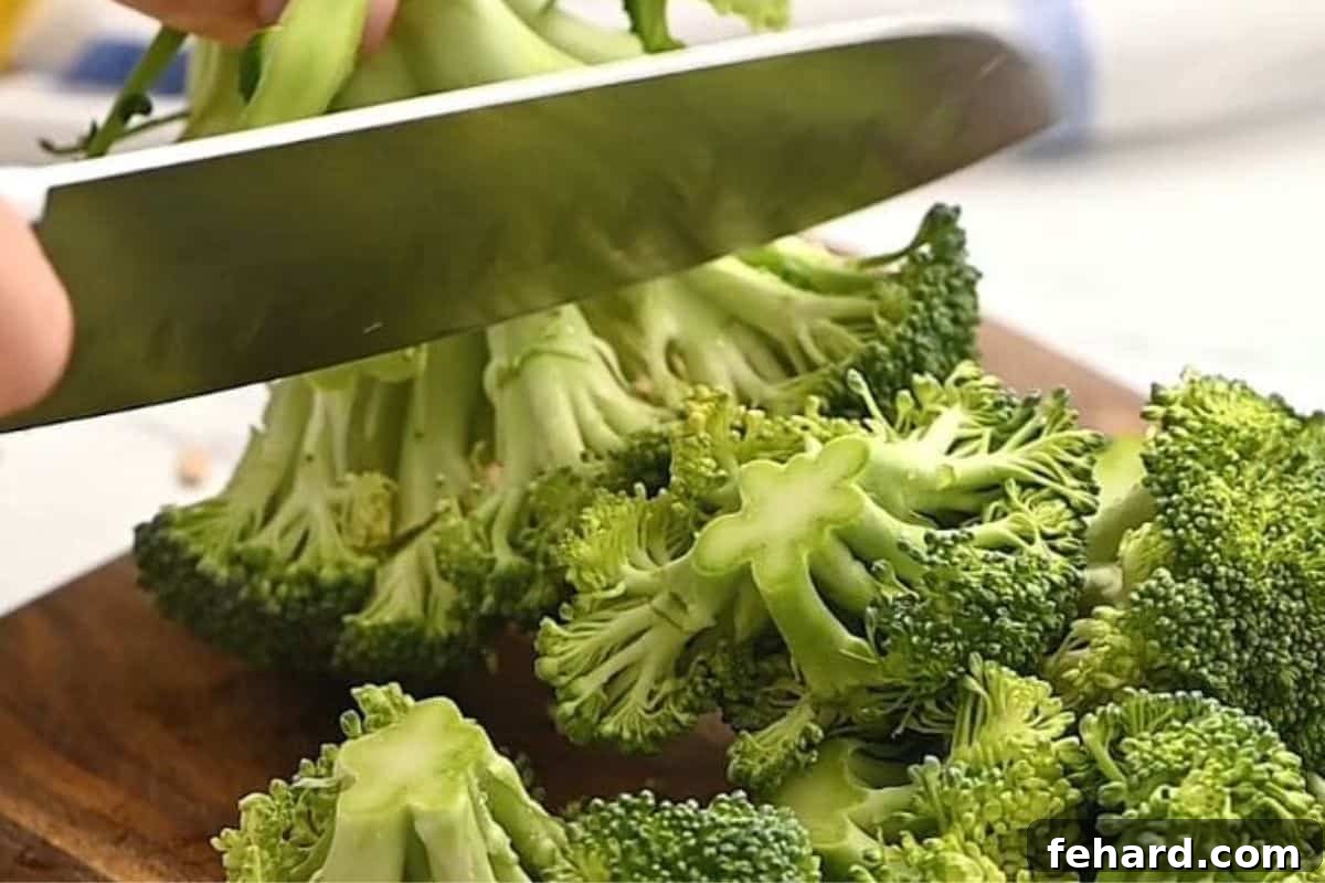 A knife expertly cutting broccoli florets from the main stem on a cutting board, demonstrating the first step in preparing broccoli for the salad.
