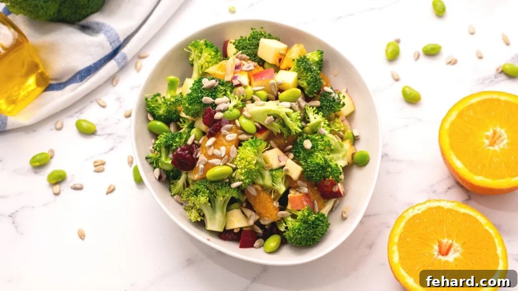 A beautifully presented bowl of healthy Broccoli Apple Salad, garnished with sunflower seeds, next to fresh oranges on a rustic wooden surface, highlighting its freshness and appeal.