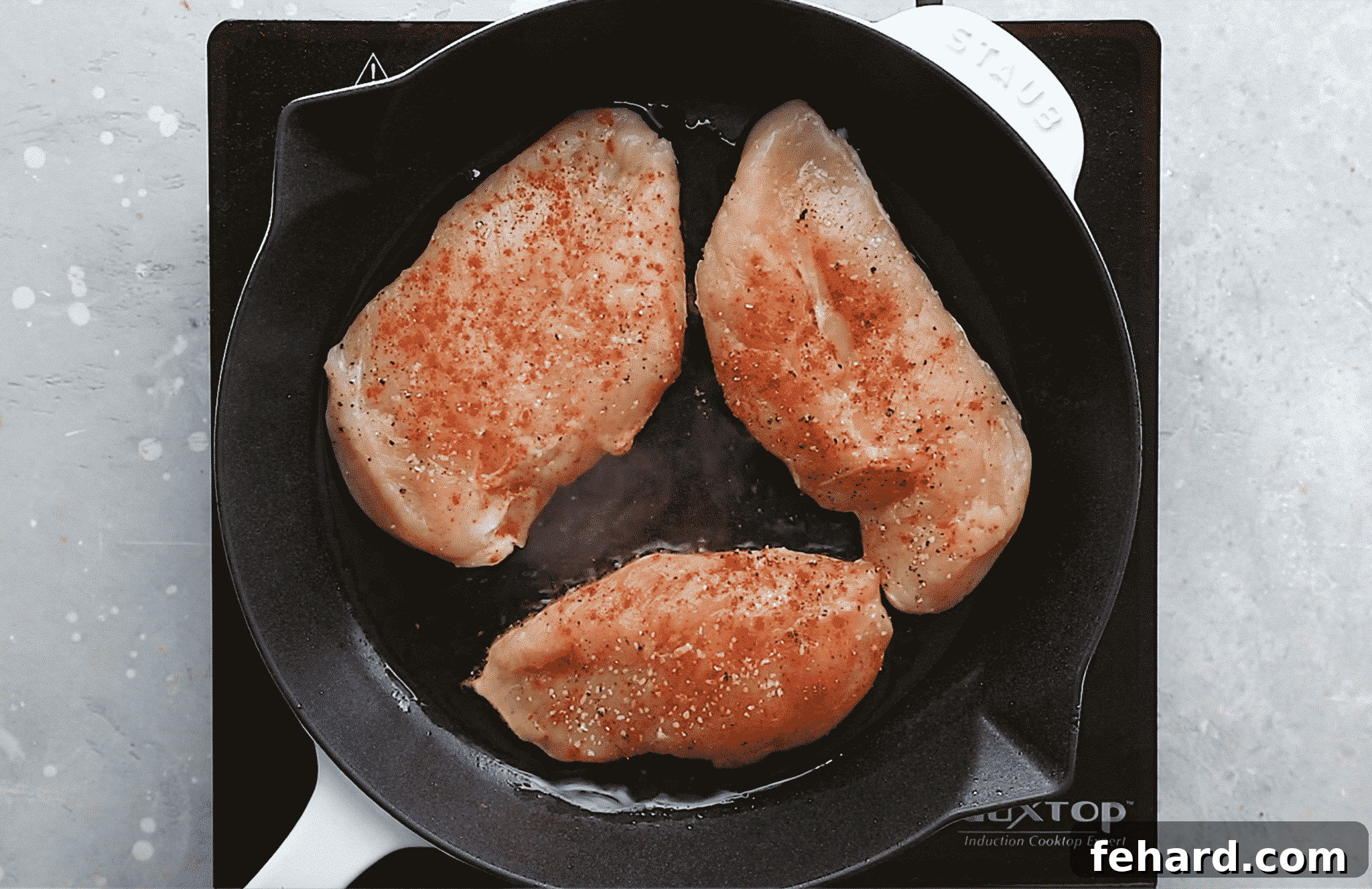 Overhead view of a cast iron skillet containing raw chicken breast