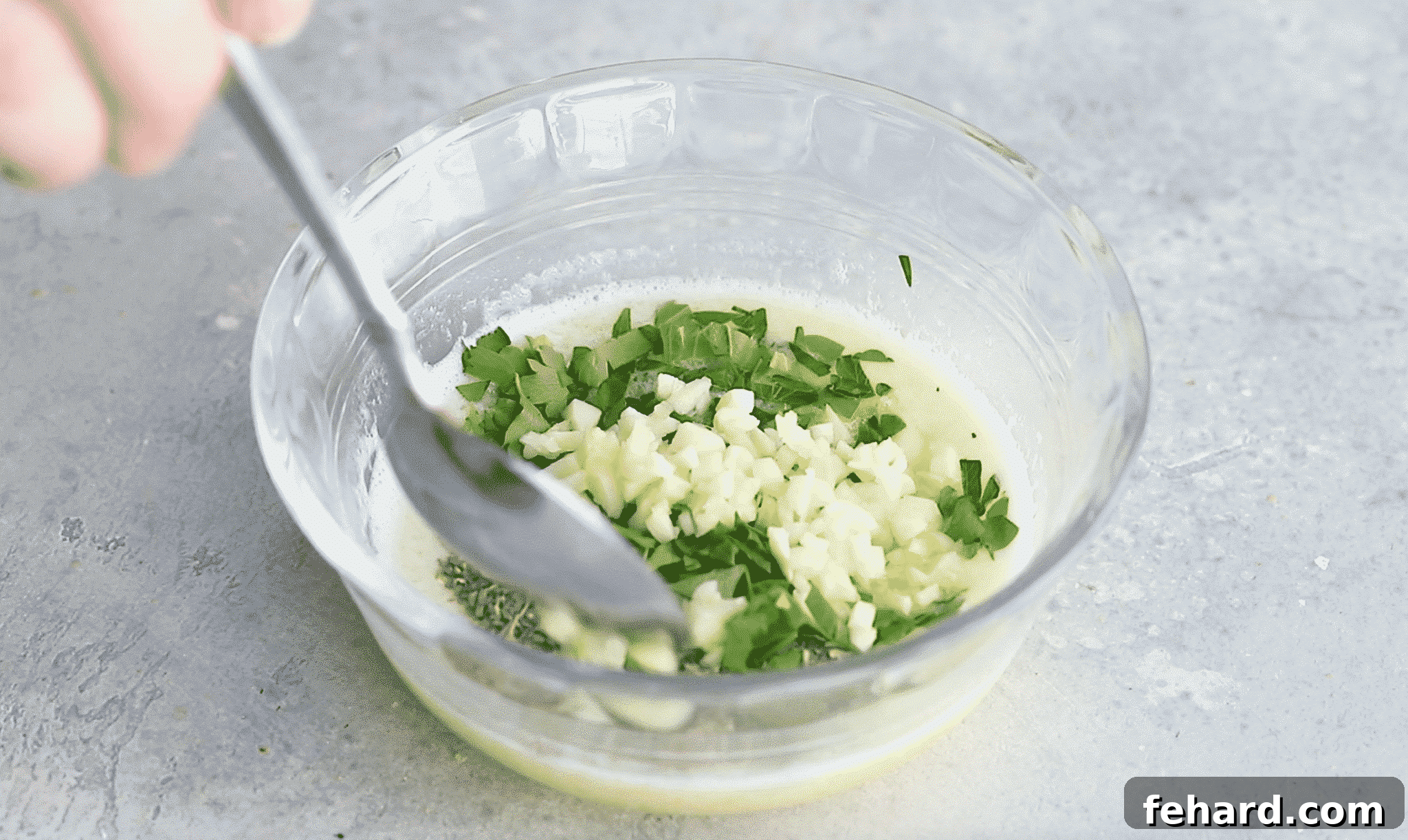 A small glass bowl of melted butter, garlic and parsley