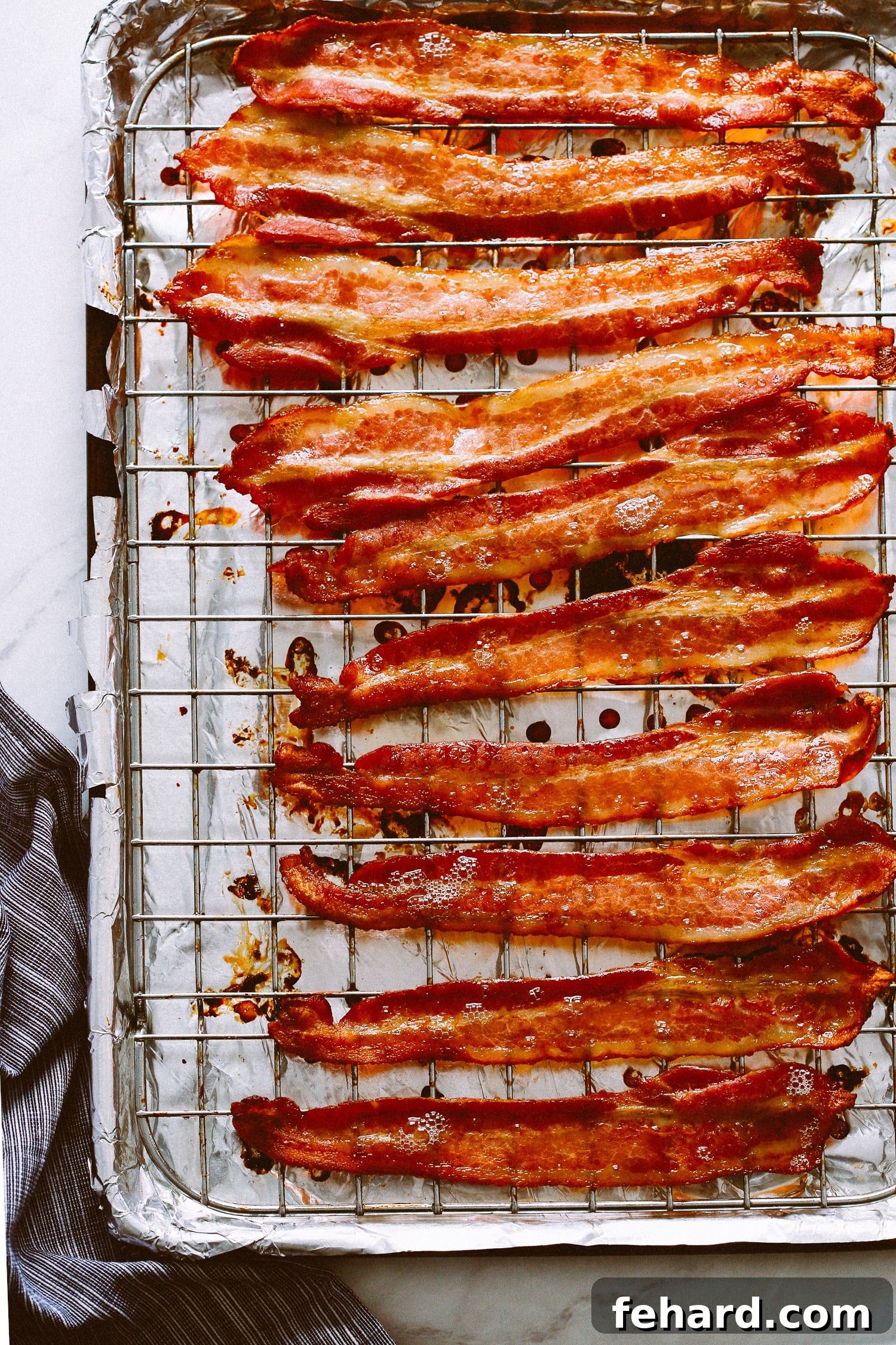 Cooked bacon on a wire rack atop a foil lined baking sheet, golden and crisp.