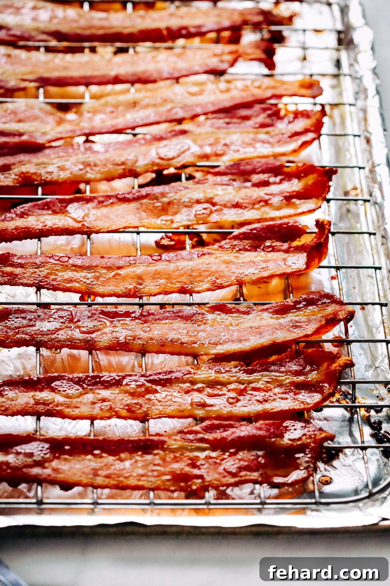 Raw bacon slices arranged neatly on a wire rack atop a foil-lined baking sheet, ready for the oven.