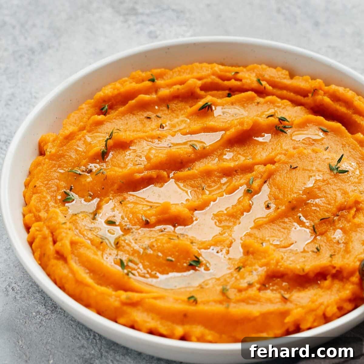 Easter Goodness Guilt Free 3 A close-up of a pristine white bowl containing velvety smooth mashed sweet potato, garnished with fresh herbs.