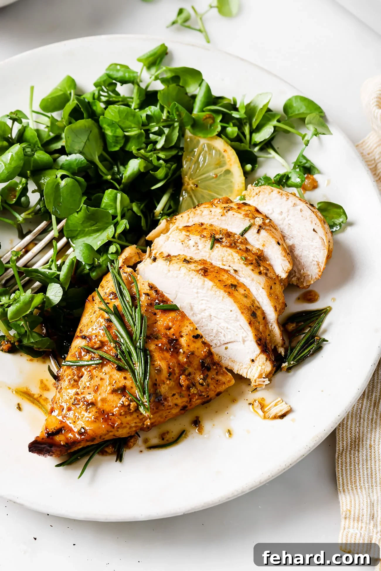 Sliced lemon rosemary chicken on a plate with a green salad.