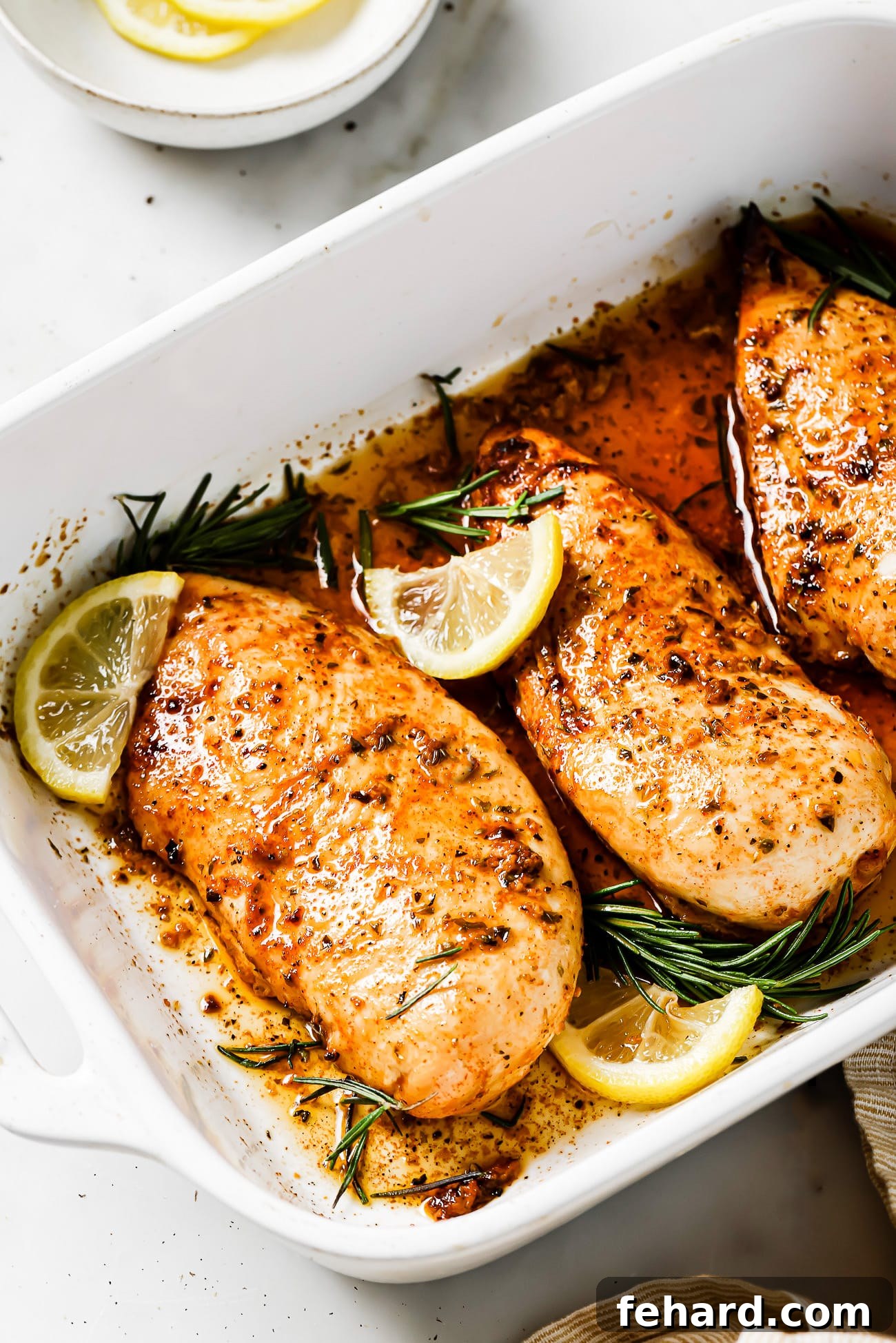 A casserole dish with lemon rosemary chicken garnished with lemon slices and rosemary sprigs.