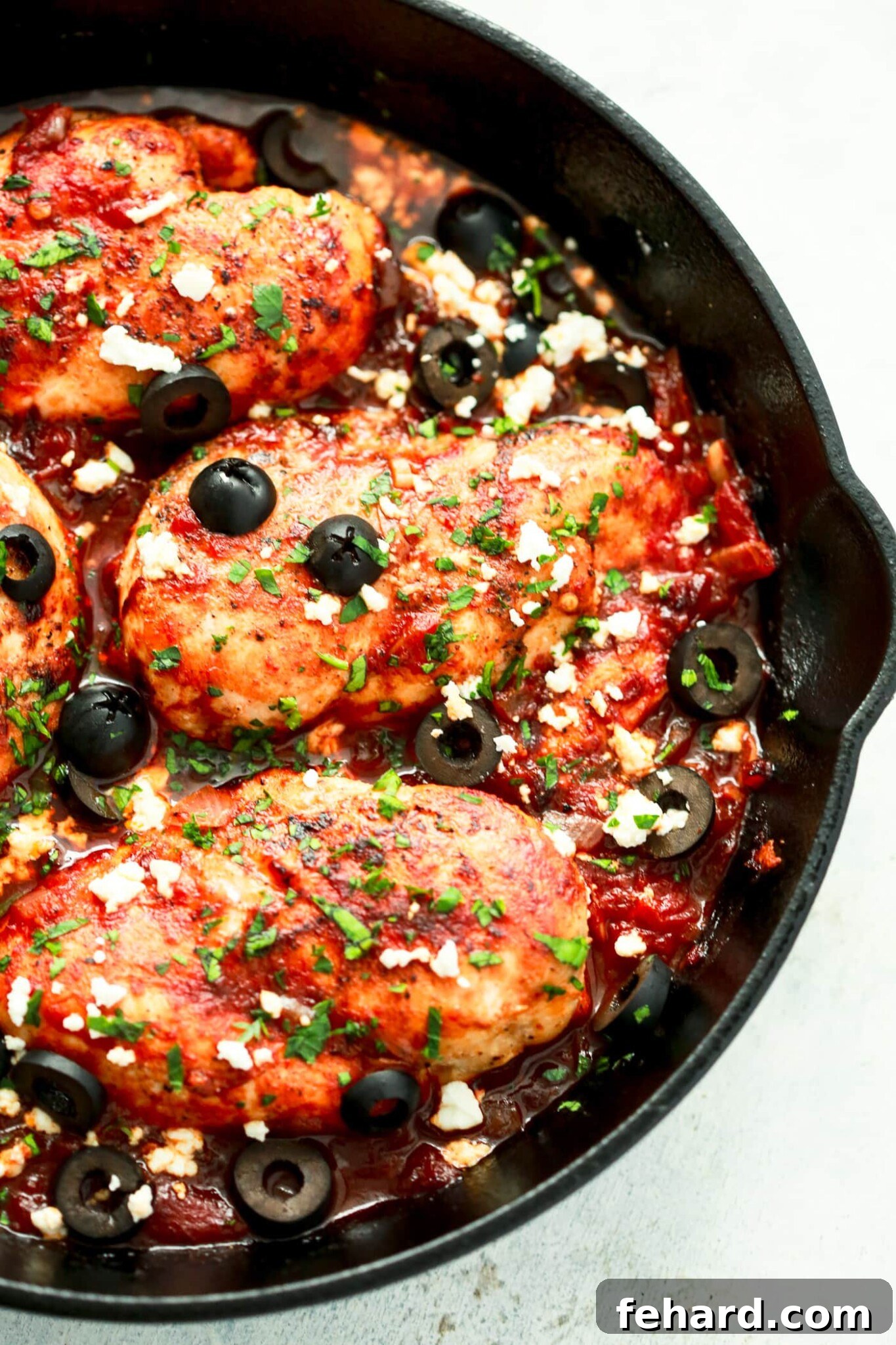 Mediterranean chicken cooked in a cast iron skillet, with olives, feta, and tomatoes, bubbling in a rich sauce.