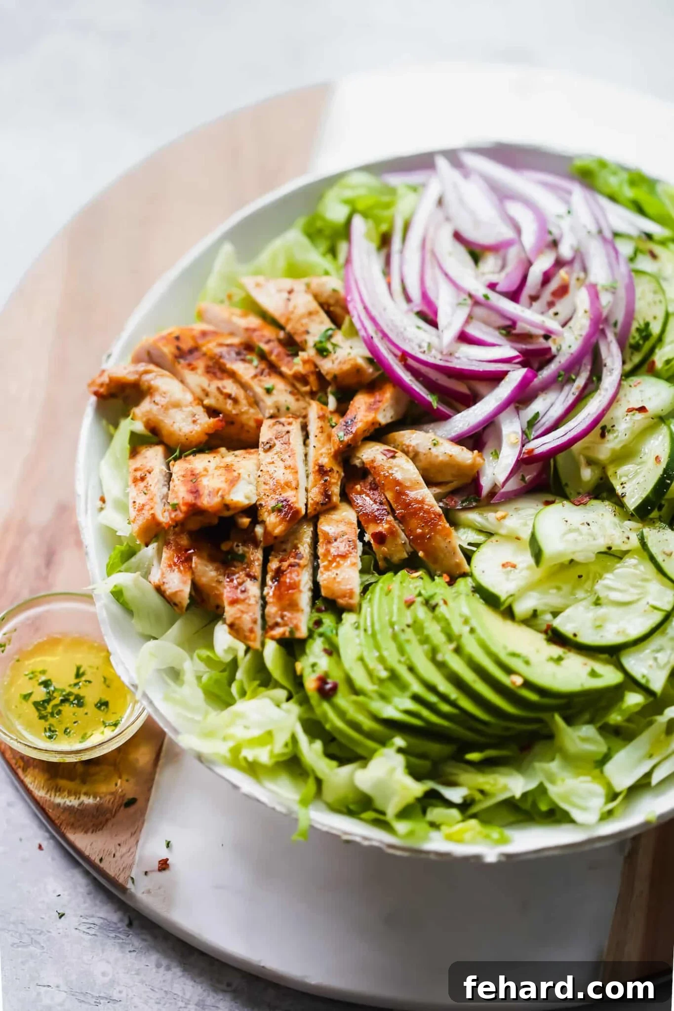 Grilled avocado chicken salad presented in a white bowl, garnished with fresh herbs and lemon wedges.
