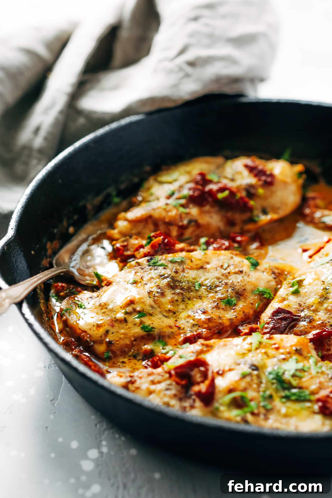 Creamy parmesan chicken simmering in a cast iron skillet, topped with fresh parsley and ready to serve.