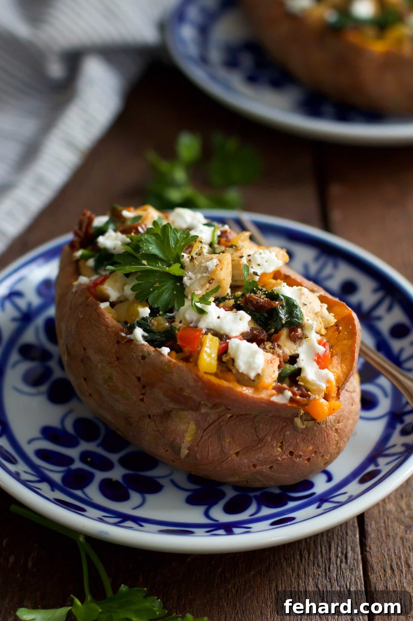 A baked sweet potato generously stuffed with goat cheese, chicken, and vegetables, presented on a plate.