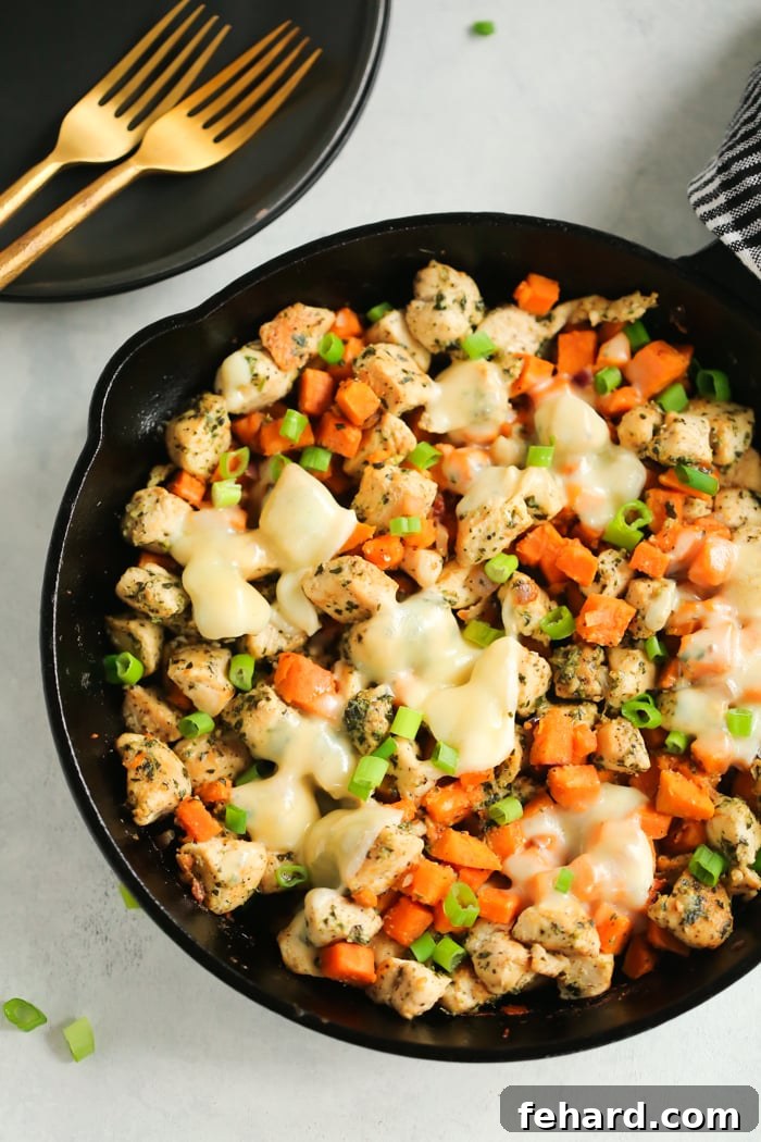 Sweet potato pesto chicken bubbling in a cast iron skillet, topped with melted mozzarella cheese and fresh basil.