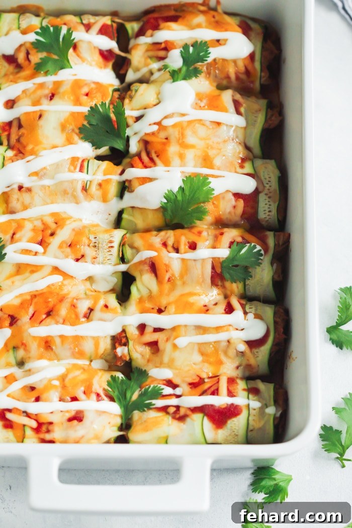 Zucchini enchiladas with chicken, baked to perfection in a white baking dish, topped with melted cheese and sauce.