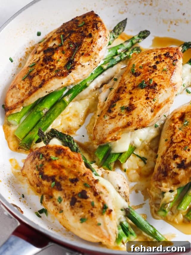 Overhead view of asparagus stuffed chicken breast in a white skillet, garnished with fresh lemon slices and herbs.