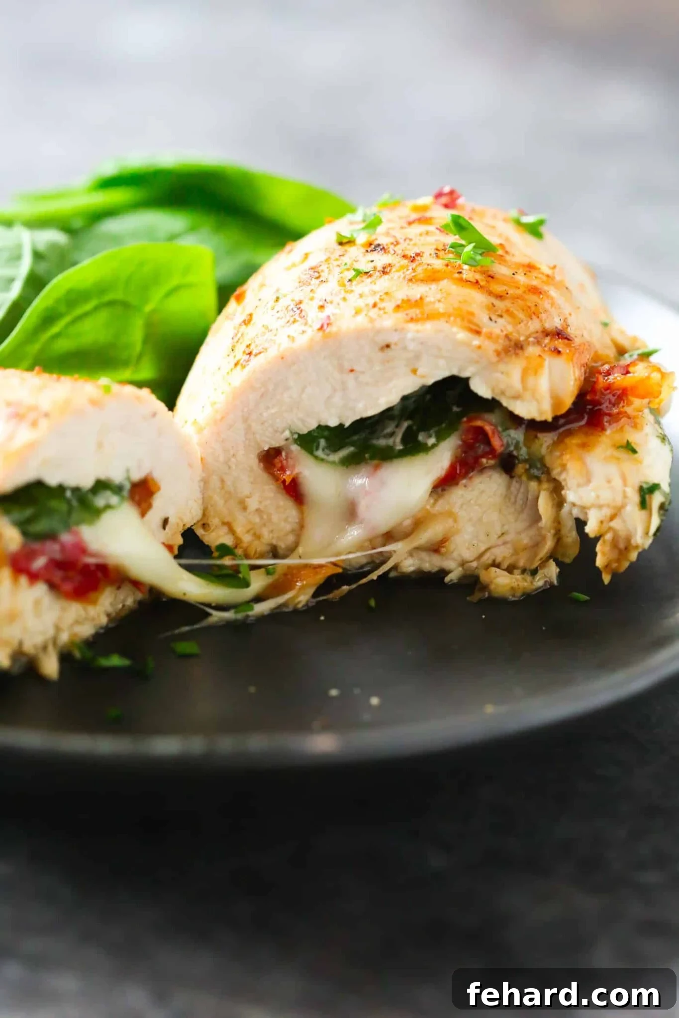 Close-up of a perfectly cooked sun-dried tomato, spinach, and cheese stuffed chicken breast on a black plate, showcasing its golden exterior and rich filling.