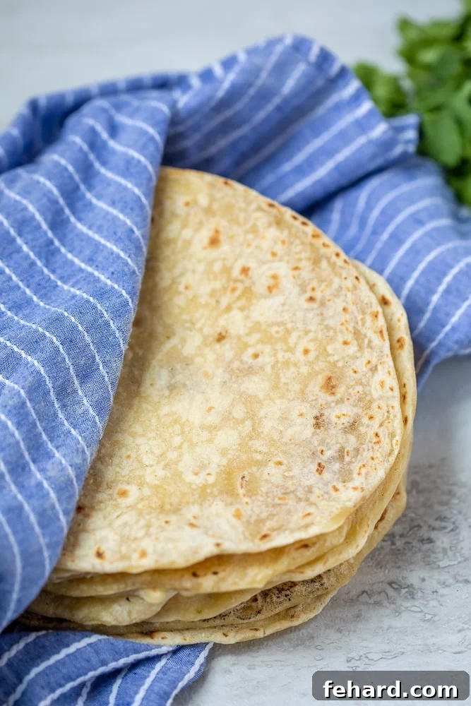 Freshly made homemade flour tortillas stacked on a blue cloth, ready to be enjoyed.