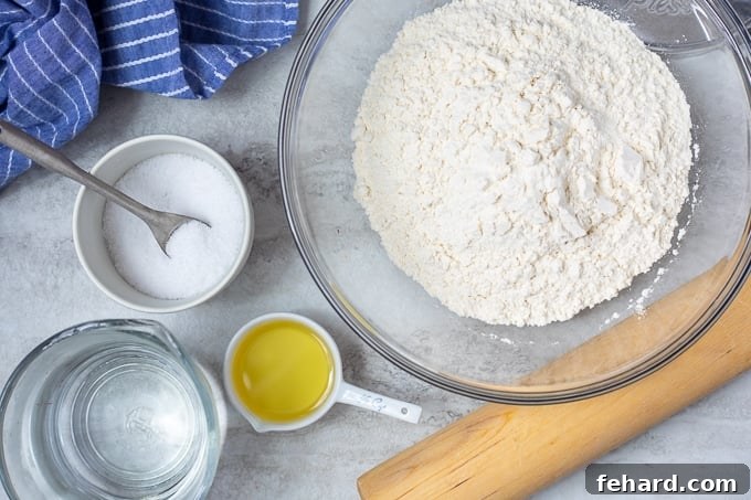 Four simple ingredients for flour tortillas displayed on a white counter: flour, salt, oil, and warm water.
