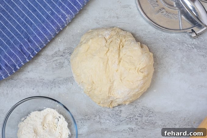 Resting tortilla dough ball next to a small bowl of flour on a floured surface.