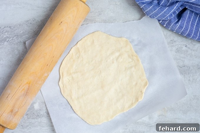 A rolled-out flour tortilla dough on parchment paper, ready for cooking.