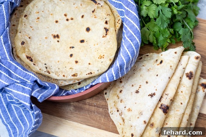 Stack of warm, freshly made homemade tortillas on a cutting board, covered with a towel.