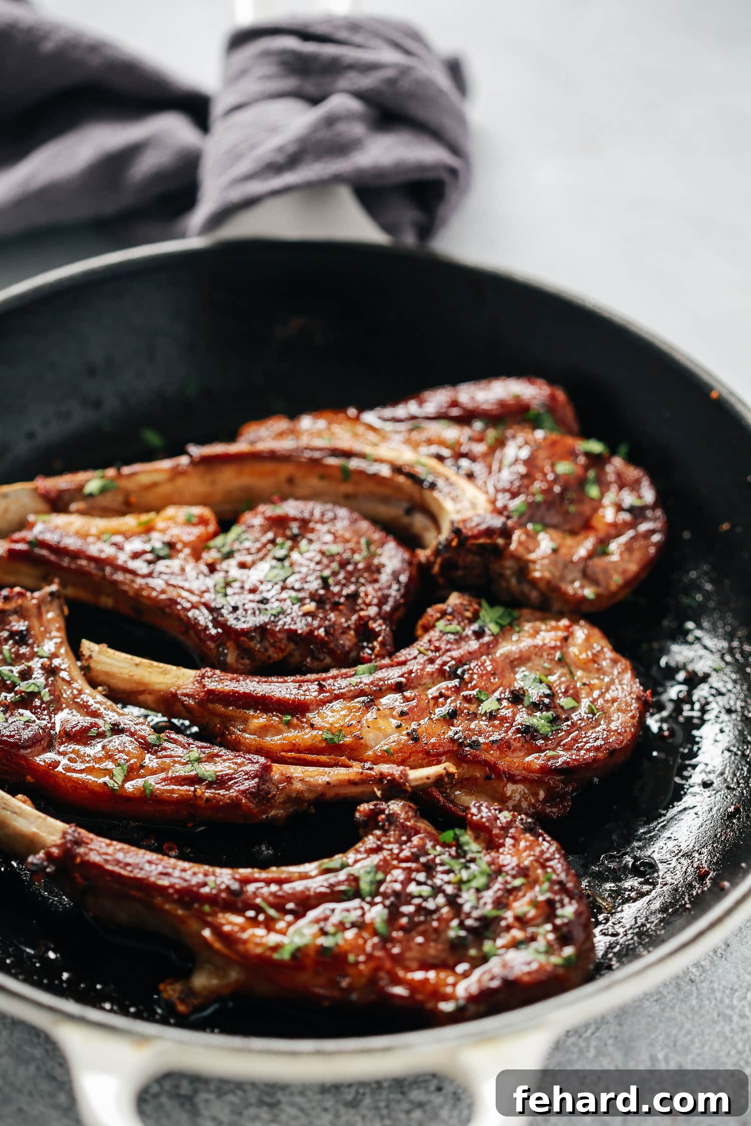 Overhead view of a skillet containing garlic butter lamb chops, perfectly seared and glistening with butter, garlic, and thyme.