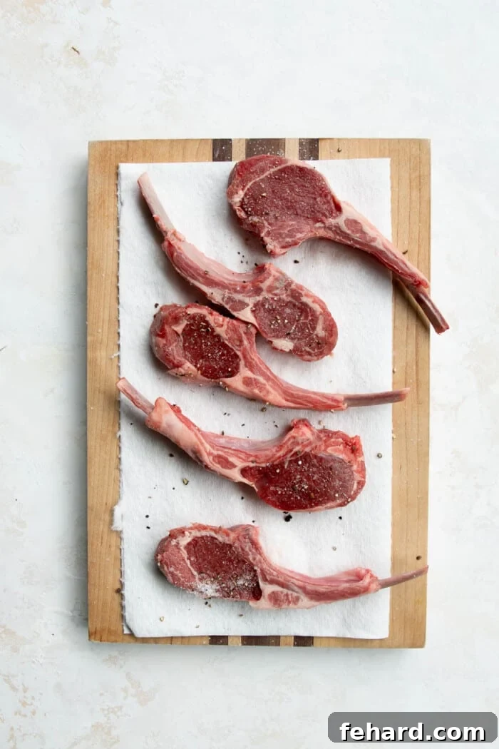 Raw lamb loin chops seasoned with salt and pepper on a wooden board, ready for searing.