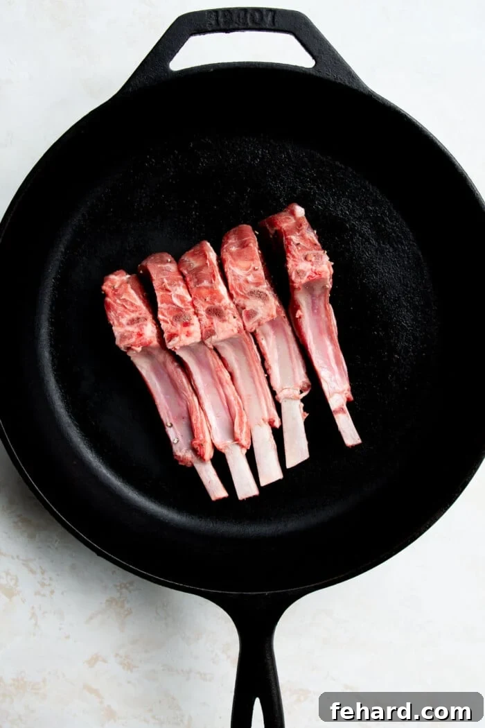 Raw lamb chops with the narrow fat side down in a hot cast iron skillet, rendering fat.